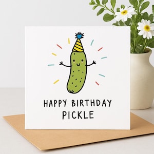 May include: A white birthday card with the words "HAPPY BIRTHDAY PICKLE". The card shows a cartoon pickle wearing a party hat and radiating colourful lines. The card is on a brown envelope.