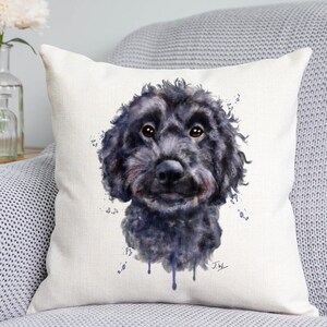 May include: A square throw pillow with a white background featuring a watercolour-style illustration of a fluffy black dog's head. The artwork includes blue paint splatters and drips, with the initials J.W. signed in the bottom right corner.