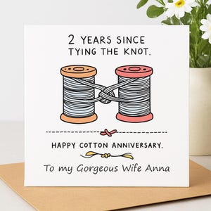 May include: A square greeting card with a white background featuring an illustration of two thread spools, one orange and one pink, tied together with a knot. The text reads: 2 YEARS SINCE TYING THE KNOT. HAPPY COTTON ANNIVERSARY. To my Gorgeous Wife Anna.