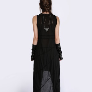 May include: A black sleeveless maxi dress with a geometric pendant necklace. The dress has a high neckline and a flowing skirt.