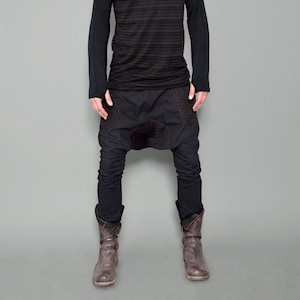 May include: A man wearing a black long-sleeved shirt with a mesh pattern and black pants with a unique design. He is wearing brown boots.