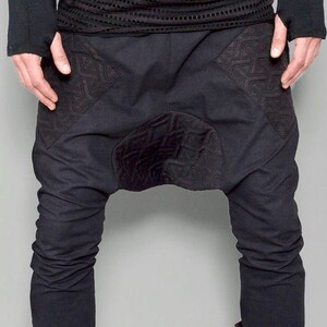 May include: Black pants with a unique design featuring embroidered details and a gathered crotch. The pants are made of a soft, comfortable fabric and have a relaxed fit.