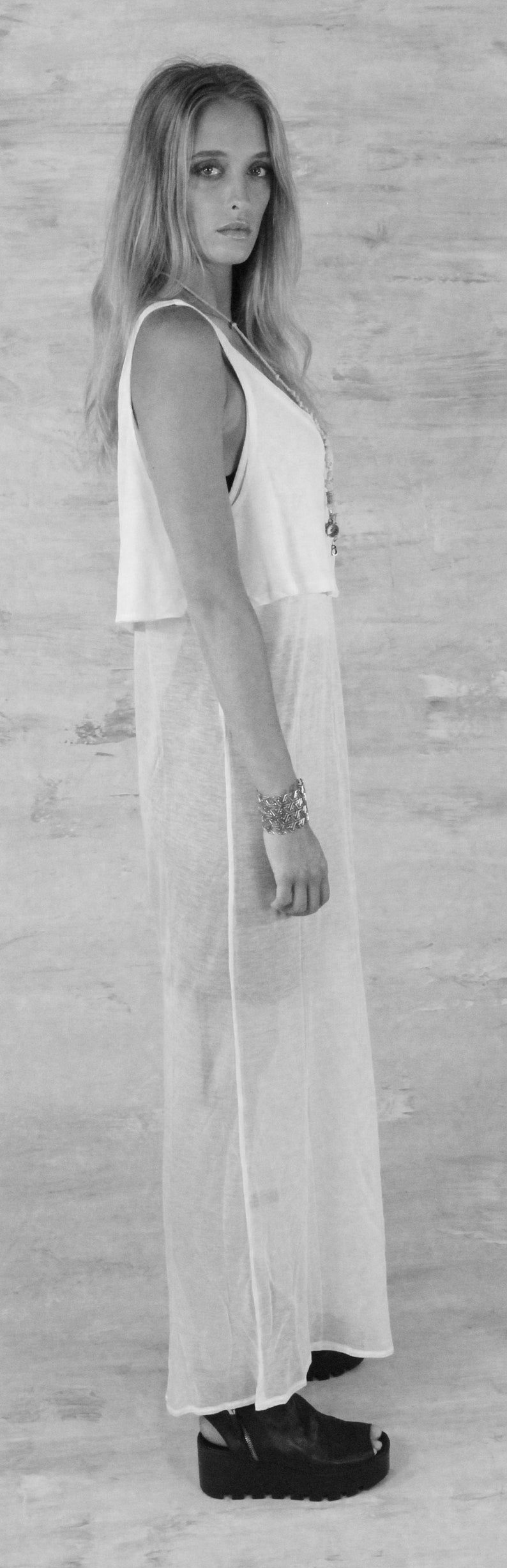 May include: A woman wearing a white sleeveless top with a sheer overlay and a silver chain necklace. She is wearing a silver bracelet on her wrist and black platform sandals.