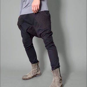 May include: A pair of black pants with a unique design featuring geometric patterns on the front. The pants are worn with gray suede ankle boots.