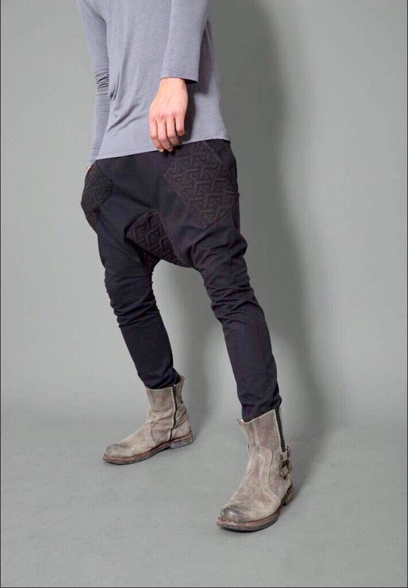 May include: A pair of black pants with a unique design featuring geometric patterns on the front. The pants are worn with gray suede ankle boots.