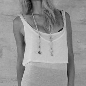 May include: A woman wearing a white sleeveless top with a beaded necklace and a white skirt.