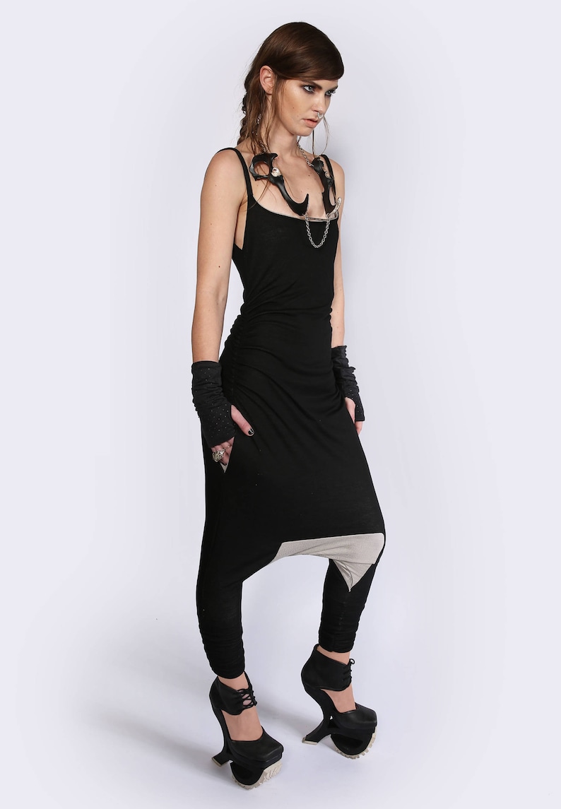 May include: A woman wearing a black jumpsuit with a white panel on the leg. She is wearing black gloves and black platform shoes.