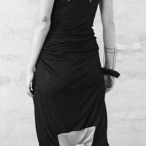 May include: A black and white photo of a person wearing a black jumpsuit with a loose fit and a low crotch. The jumpsuit has a white panel on the back. The person is wearing black platform sandals.