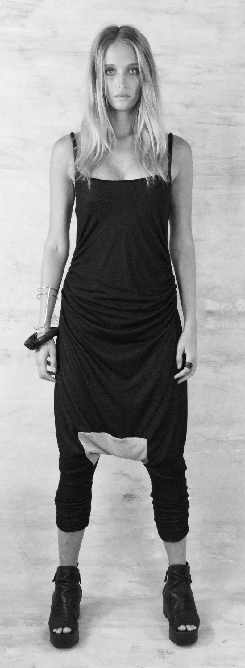 May include: A black and gray jumpsuit with a draped design. The jumpsuit has a scoop neck and thin straps. The model is wearing black platform sandals.