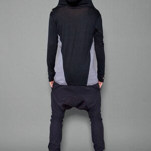 May include: A black hooded long-sleeve shirt with a gray panel on the back. The shirt is paired with black pants that have a unique design on the knees.
