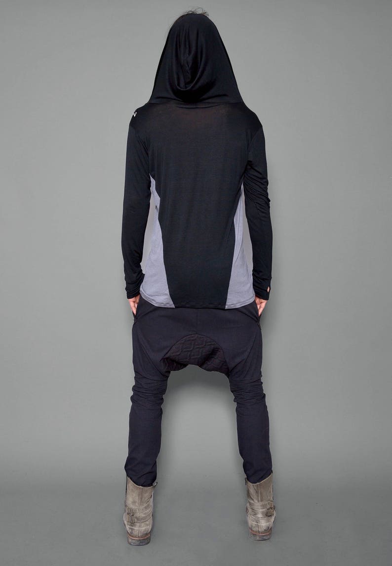 May include: A black hooded long-sleeve shirt with a gray panel on the back. The shirt is paired with black pants that have a unique design on the knees.