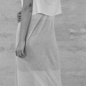 May include: A woman wearing a white sheer maxi dress with a white tank top underneath. She is wearing black platform sandals.