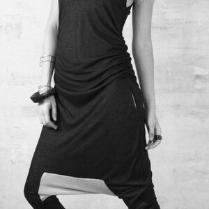 May include: A black and grey jumpsuit with a loose fit and a drawstring waist. The jumpsuit has a unique design with a split at the bottom of the legs. The model is wearing black platform sandals.