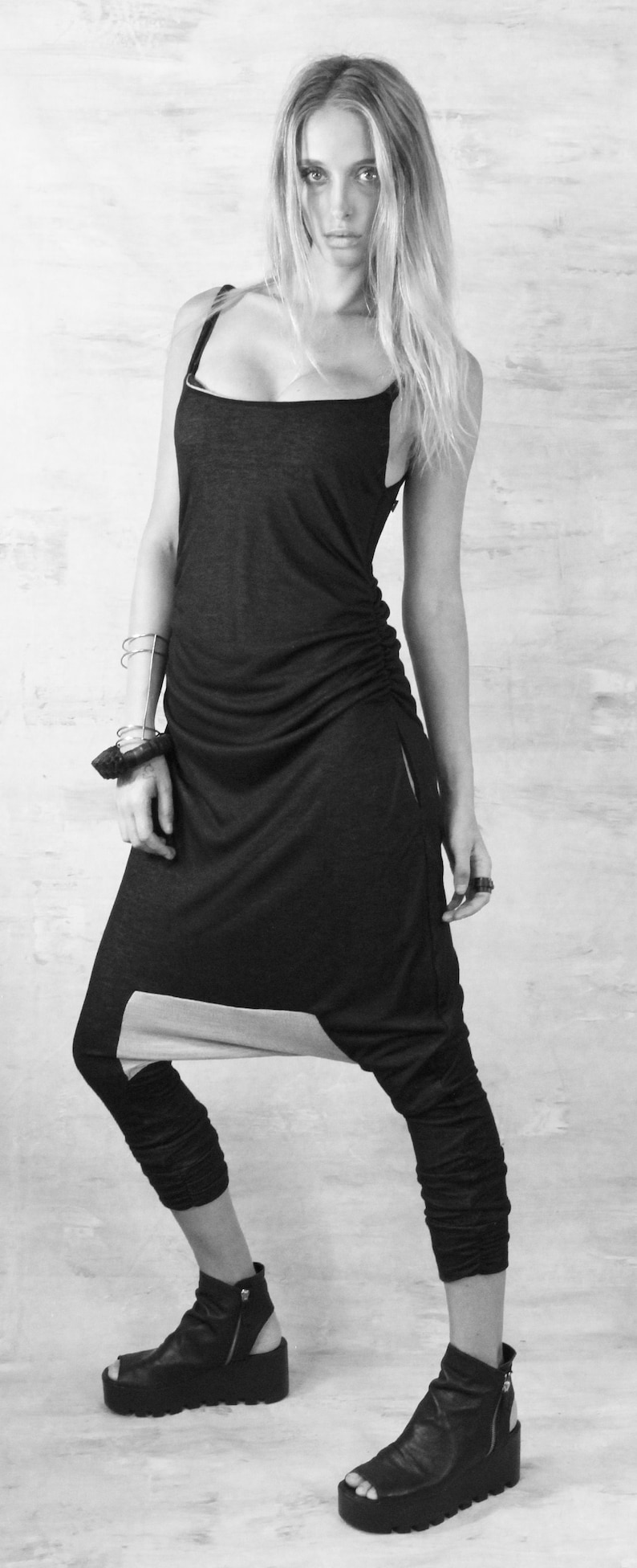 May include: A black and grey jumpsuit with a loose fit and a drawstring waist. The jumpsuit has a unique design with a split at the bottom of the legs. The model is wearing black platform sandals.