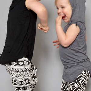 May include: Two children wearing hooded shirts and black and white patterned pants. The child on the left is wearing a black hooded shirt and the child on the right is wearing a gray hooded shirt.