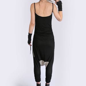May include: A black jumpsuit with a low-cut back and a gathered waist. The jumpsuit has a unique design with a white panel at the crotch. The model is wearing black heeled shoes.