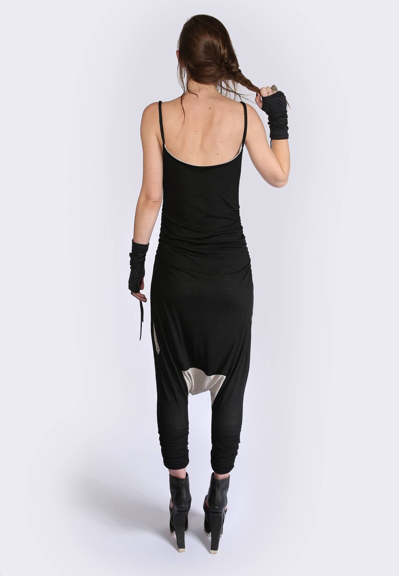 May include: A black jumpsuit with a low-cut back and a gathered waist. The jumpsuit has a unique design with a white panel at the crotch. The model is wearing black heeled shoes.