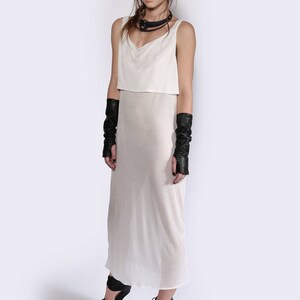 May include: A white sleeveless dress with a sheer overlay and a black choker necklace. The model is wearing black leather fingerless gloves and black platform shoes.