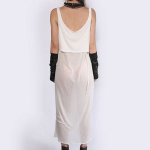 May include: A white sheer maxi dress with a white tank top layered over it. The dress has a thin black strap around the neck and the model is wearing black fingerless gloves.