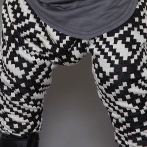 May include: Black and white checkered pattern pants with a gray shirt tucked in. The pants have a geometric pattern.