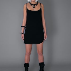 May include: A black sleeveless mini dress with a scoop neck and a side slit. The model is wearing black platform boots and a silver choker necklace.