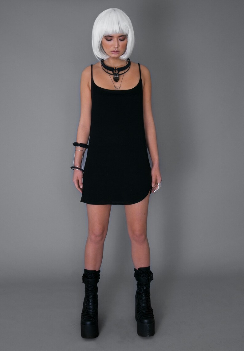 May include: A black sleeveless mini dress with a scoop neck and a side slit. The model is wearing black platform boots and a silver choker necklace.
