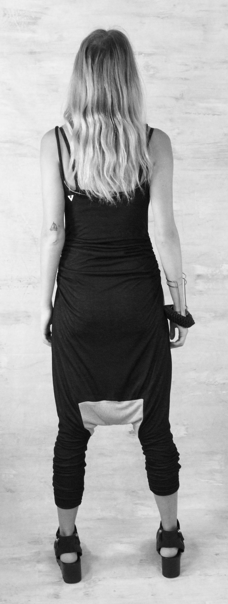 May include: A black jumpsuit with a white panel on the back. The jumpsuit has a loose fit and is made of a soft, stretchy fabric. The model is wearing the jumpsuit with a pair of black sandals.