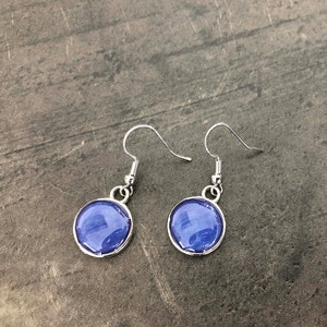 Peut inclure: Une paire de boucles d'oreilles pendantes en argent avec des cabochons ronds en verre bleu.