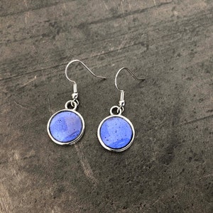 Peut inclure: Une paire de boucles d'oreilles pendantes en argent avec des pierres rondes en verre bleu. Les pierres ont un motif moucheté.