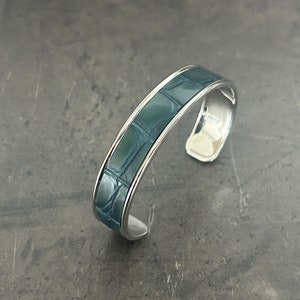 Op de afbeelding: Een zilveren armband met een donkerblauwe inleg van alligatorleer.