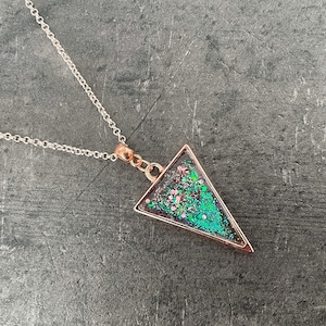 May include: A silver chain necklace with a rose gold triangle pendant filled with green and pink glitter.