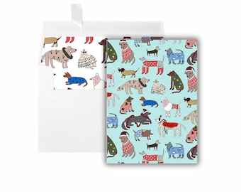 Könnte beinhalten: Eine blaue und weiße Karte mit einem Muster aus Hunden, die Weihnachtspullover tragen. Die Hunde sind in verschiedenen Posen und Rassen dargestellt. Die Karte ist innen leer und wird mit einem weißen Umschlag geliefert.