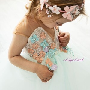 May include: A little girl wearing a light blue tulle dress with floral embroidery. The dress has a sweetheart neckline and cap sleeves. The girl is wearing a pink flower crown.