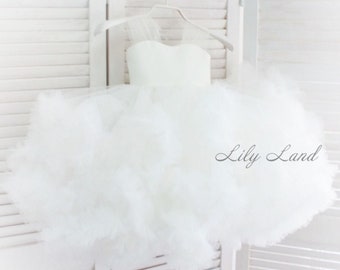 May include: A white tulle dress with a fluffy, layered skirt. The dress has a strapless bodice and a sheer overlay. The dress is hanging on a hanger against a white background. The text "Lily Land" is visible in the bottom right corner of the image.