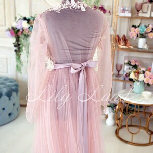 May include: A pink tulle gown with a white lace bodice and a matching satin sash. The gown is on a mannequin and has long sleeves.