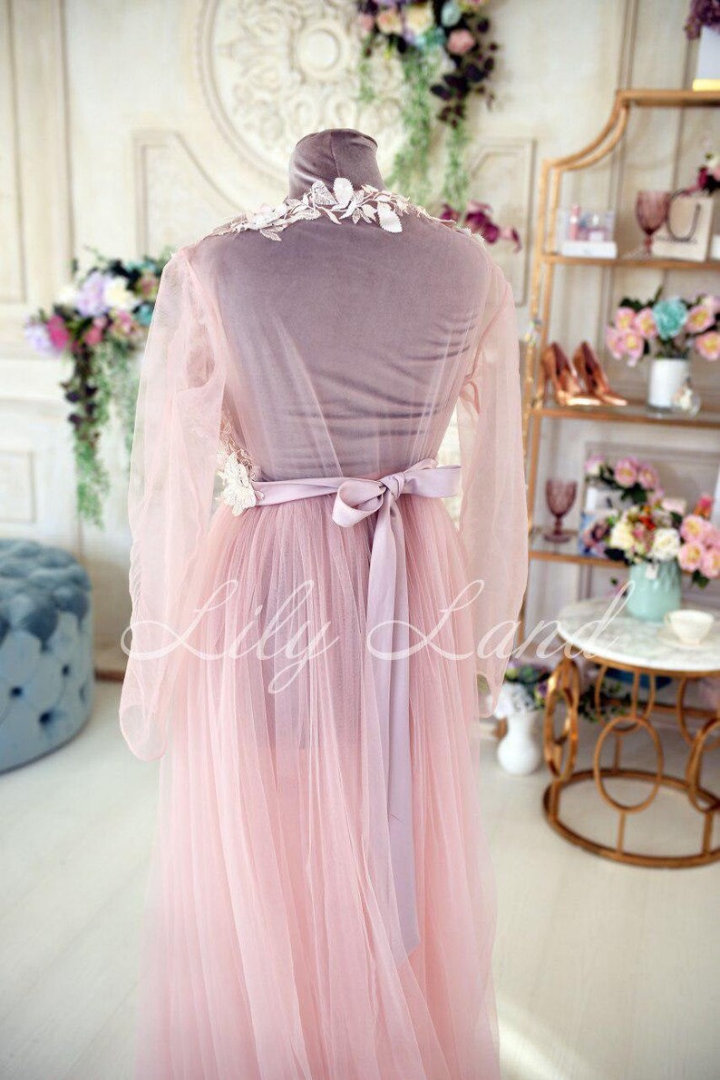May include: A pink tulle gown with a white lace bodice and a matching satin sash. The gown is on a mannequin and has long sleeves.