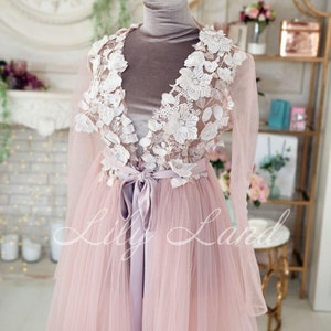 May include: A long, pink tulle gown with a white lace overlay and a satin sash. The lace features delicate floral designs. The gown is on a mannequin.
