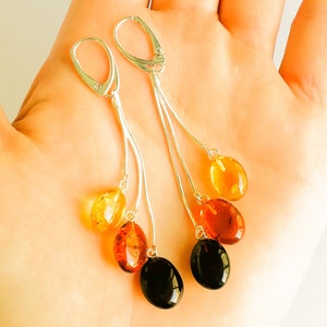 Può includere: Orecchini pendenti in argento con tre pietre di ambra in tonalità di giallo, arancio e nero.