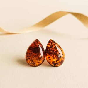 May include: A pair of amber teardrop earrings with a natural, organic look. The earrings are a warm, honey-brown color with flecks of gold throughout.