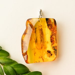 May include: A large, amber-colored pendant with a silver bail. The amber is translucent and has a natural, organic shape. The pendant is approximately 2 inches in length.