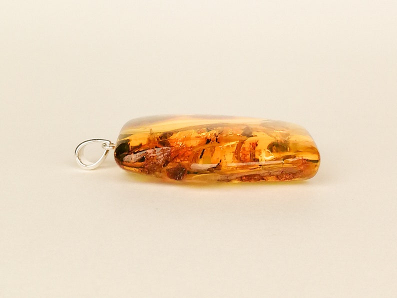 May include: A rectangular amber pendant with a silver bail. The amber is a warm honey color and has inclusions of plant material.