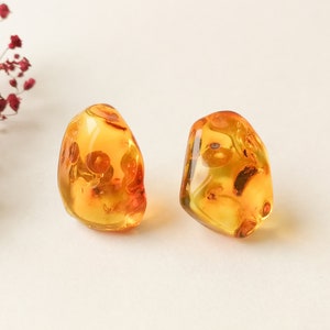 May include: A pair of amber earrings with inclusions. The earrings are a light amber colour and have a smooth, polished finish.