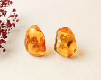 May include: A pair of amber earrings with inclusions. The earrings are a light amber color and have a smooth, polished finish.