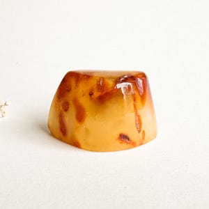 May include: A translucent, amber-coloured decorative object with dark brown inclusions. The object has a rounded, irregular shape and a glossy finish. The item is likely a decorative piece or a small sculpture.