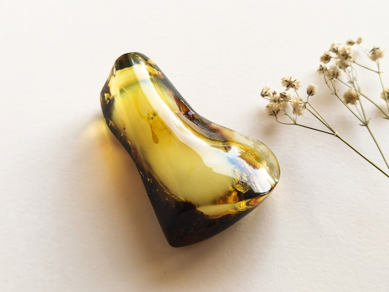 May include: A large, irregular, yellow amber stone with a smooth, polished surface. The stone has a light yellow color with darker brown streaks and inclusions.