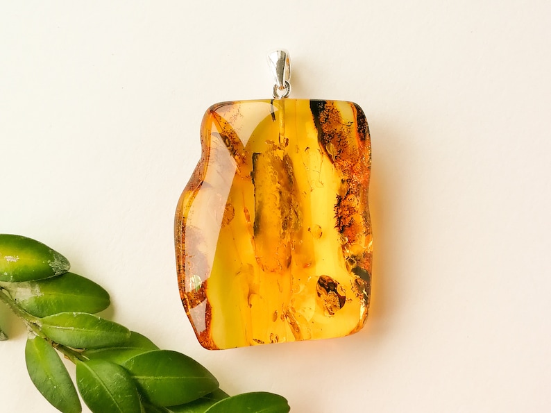 May include: A large, amber-colored pendant with a silver bail. The amber is translucent and has a natural, organic shape. The pendant is approximately 2 inches in length.