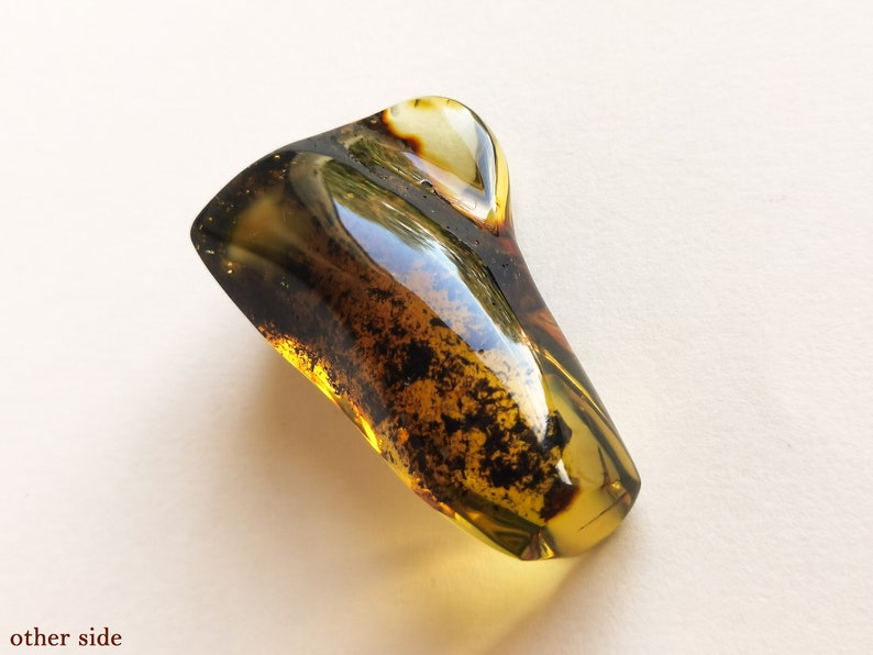 May include: A large, irregularly shaped piece of amber with a dark brown and green color. The amber has a smooth, polished surface and contains small black inclusions.
