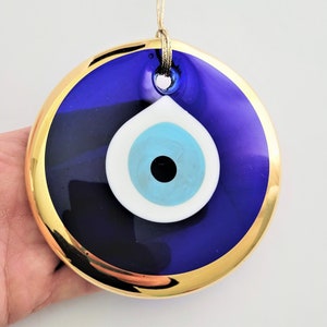 May include: A round blue evil eye charm with a gold rim and a white eye with a blue iris and a black pupil. The charm is hanging from a string.