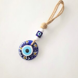 May include: Blue evil eye charm with white flowers and a blue and white bead on a brown string.
