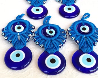 Op de afbeelding: Vijf blauwe boze oog charmes met witte en lichtblauwe centra. De charmes zijn gemaakt van glas en zijn omgeven door blauwe en witte kralen. De charmes hangen aan een blauwe string.